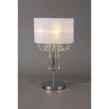 The Freida 3 Light Crystal Table Lamp features a polished chrome frame, a white shade, and sparkling crystal bead accents along the edge, shown against a plain gray background.