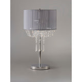 The Freida 3 Light Crystal Table Lamp features a polished chrome base, a grey shade, and decorative hanging crystals, set against a plain gray background.