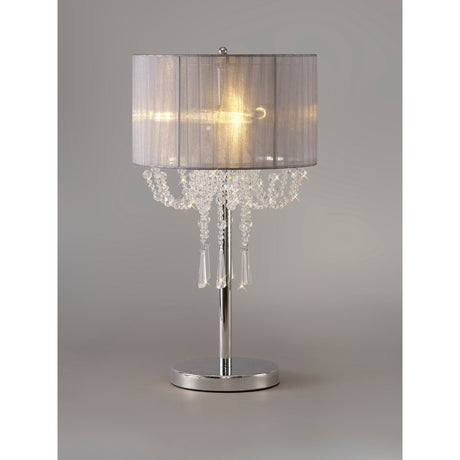 The Freida 3 Light Crystal Table Lamp features a polished chrome base, grey organza shade, and chandelier-style hanging crystal accents, illuminated against a neutral background.