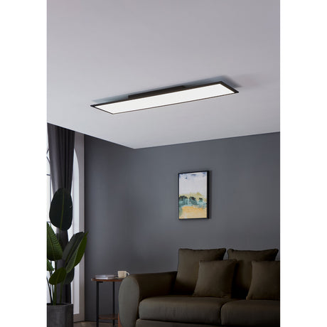 Frinarne LED Panel Light 120 x 30cm in black, a slim rectangular ceiling fixture with white diffuser, shown flush-mounted in a grey living room above a dark sofa.
