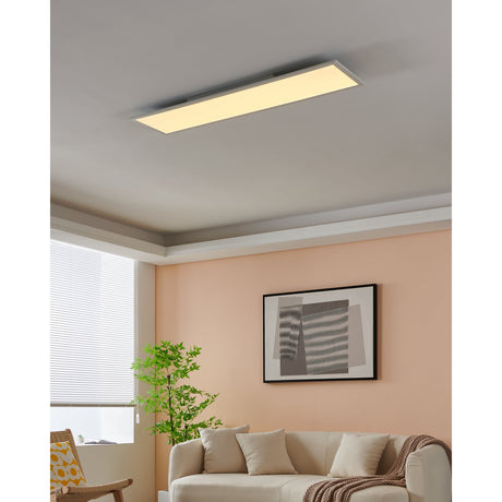 Frinarne Smart LED Panel Light 120 x 30cm in white, a slim rectangular ceiling fixture with white aluminium body, shown illuminated on a grey ceiling in a living room with a peach wall and sofa below.
