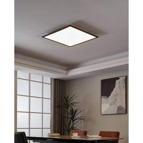 Frinarne Smart LED Panel Light, a square flush ceiling fixture with slim black aluminium frame and white diffuser, shown illuminated on a grey ceiling in a dining room.