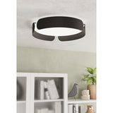 Frosmarne LED flush ceiling light in black steel with a round white diffuser and ribbon-like curved bands, shown mounted on a ceiling above a living room shelf.