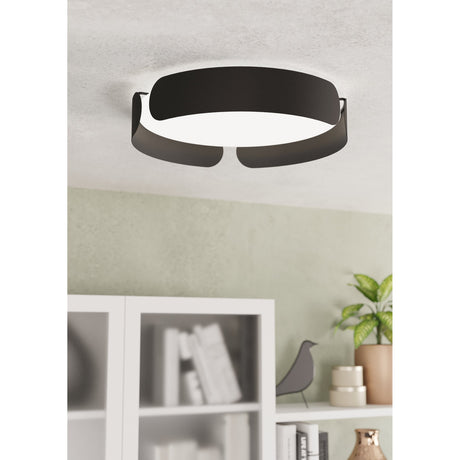 Frosmarne LED flush ceiling light in black steel with a round white diffuser and ribbon-like curved bands, shown mounted on a ceiling above a living room shelf.