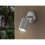 Frosmenne LED Outdoor Wall Light in stainless steel, cylindrical head on a round wall plate with adjustable joint, mounted outdoors on a textured beige wall, lit GU10 lamp visible.