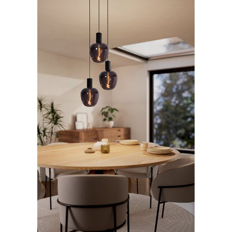 Frosvette 3 Light Pendant in black steel with round canopy and staggered cords, fitted with smoked glass globe bulbs above a wooden dining table.