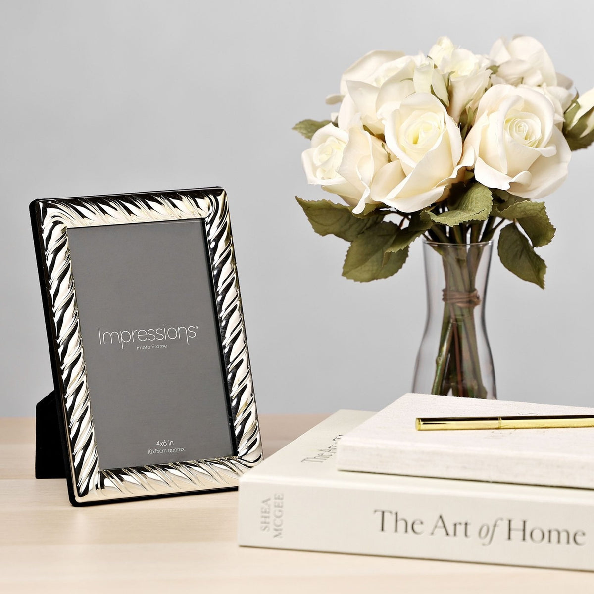 Silverplated swirl textured 4x6in photo frame with black stand on a wooden surface, styled with white roses and books in a living room setting.