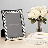 Rectangular silverplated photo frame with diagonal swirl textured border and black stand, shown on a desk beside white roses and books.