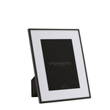 Matt black metal photo frame with white mount for a 7 x 5in rectangular print, shown at an angle with built-in stand against a plain white background.