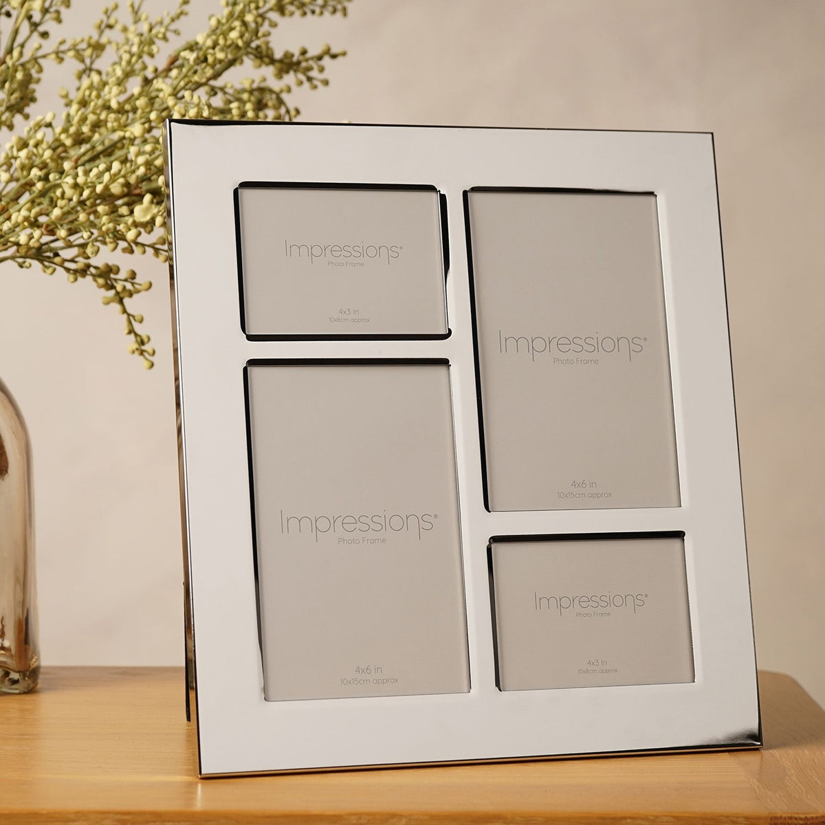 Shiny silver metal-plated 4-aperture collage photo frame with staggered rectangular openings, displayed upright on a wooden surface beside greenery.