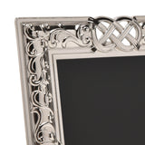 Close-up of the Celtic Knot Design Shiny Metal Photo Frame, 6 x 4in, showing silver scrollwork and interlaced knot detail on the corner, with black mat and plain white background.