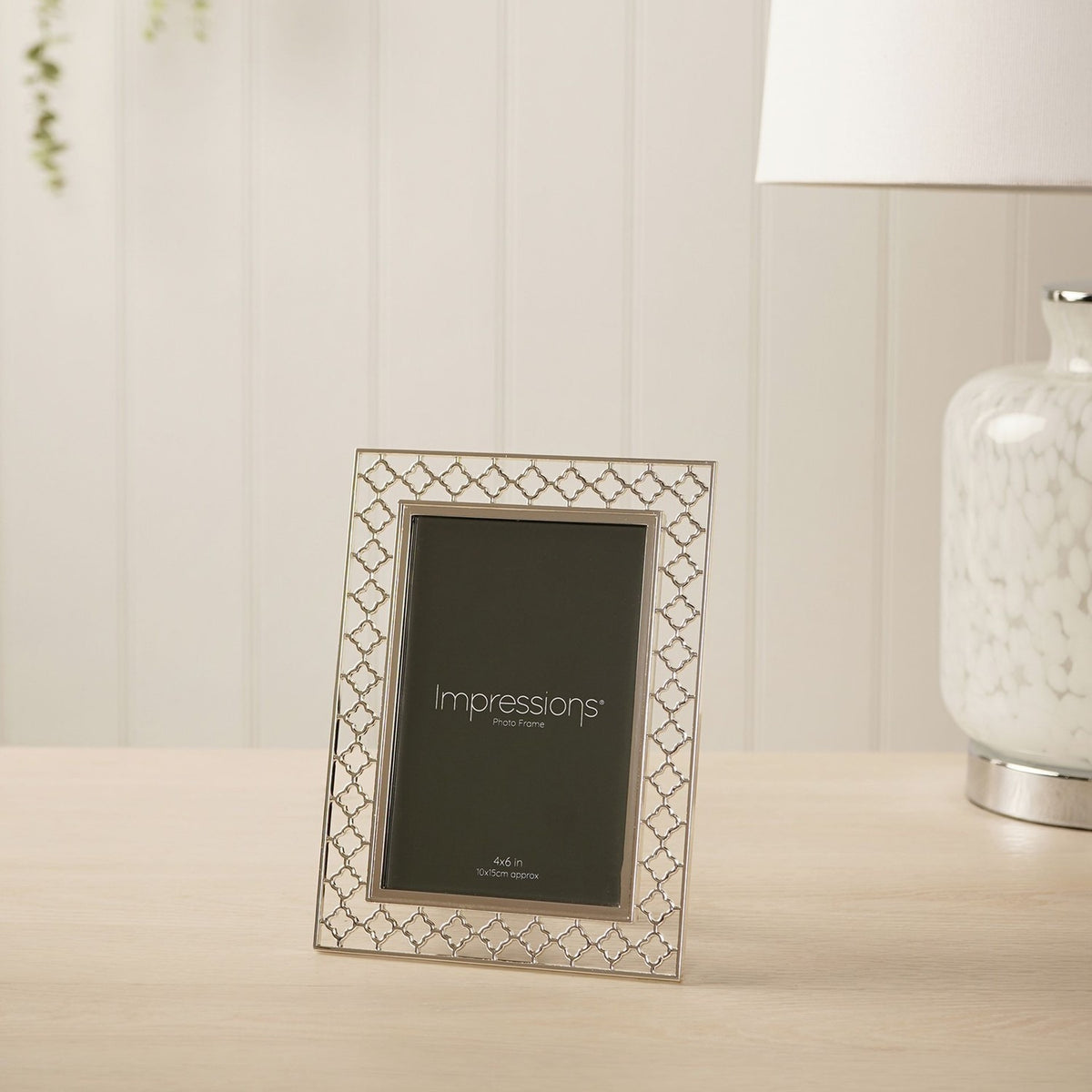 Rectangular silver-plated metal photo frame with openwork lattice border, holding a 4x6in portrait photo, displayed upright on a wooden surface.