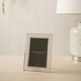 Rectangular silver-plated metal photo frame with openwork lattice border, holding a 4x6in portrait photo, displayed upright on a wooden surface.