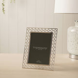 Lattice Cut Silverplated Metal Photo Frame, 7 x 5in, with openwork four-petal border and polished inner edge, displayed on a light wood surface near a table lamp.