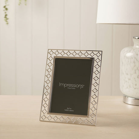 Lattice Cut Silverplated Metal Photo Frame, 7 x 5in, with openwork four-petal border and polished inner edge, displayed on a light wood surface near a table lamp.
