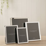 Four narrow rectangular silverplated metal photo frames in varying sizes with glossy silver borders, displayed on a wooden surface against a light panelled wall.