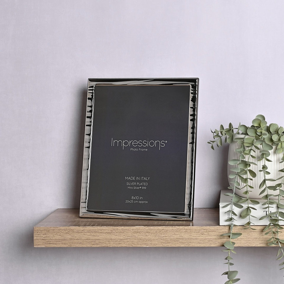 Silverplated Narrow Wave rectangular photo frame with rippled silver border, 10 x 8in opening, wood back, shown upright on a wooden shelf beside a plant.
