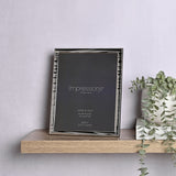 Silverplated Narrow Wave rectangular photo frame with rippled silver border, 10 x 8in opening, wood back, shown upright on a wooden shelf beside a plant.
