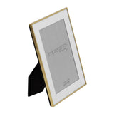 Rectangular photo frame with slim brushed brass metal border and white mount, shown at an angle with rear stand, on a plain white background.