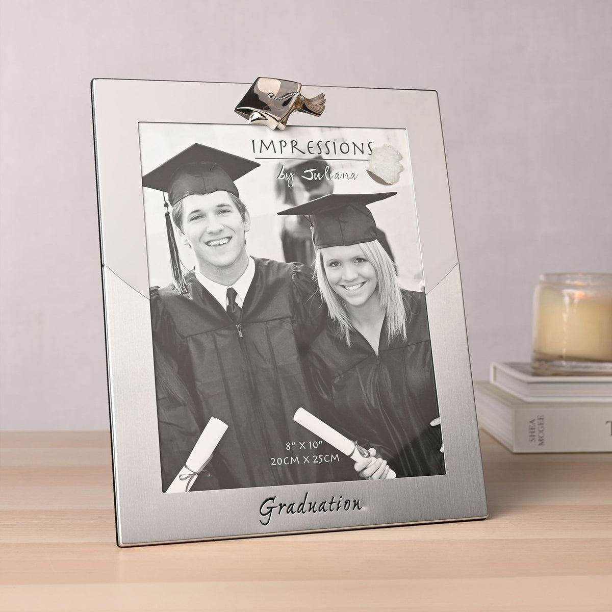 Silver two-tone metal photo frame for 10 x 8in photo, with a mortarboard cap detail on top and "Graduation" script at the base, shown on a wooden surface.