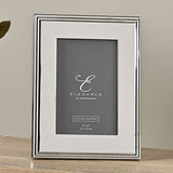 Rectangular silver-plated metal photo frame with a ribbed stepped edge and wide flat border, holding a 4" x 6" portrait photo, shown upright on a wooden surface.