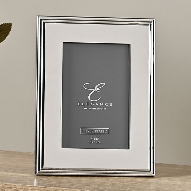 Rectangular silver-plated metal photo frame with a ribbed stepped edge and wide flat border, holding a 4" x 6" portrait photo, shown upright on a wooden surface.