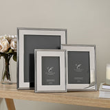 Three silverplated rectangular photo frames in graduated sizes with ribbed-edge borders, shown on a wooden table beside roses and books.
