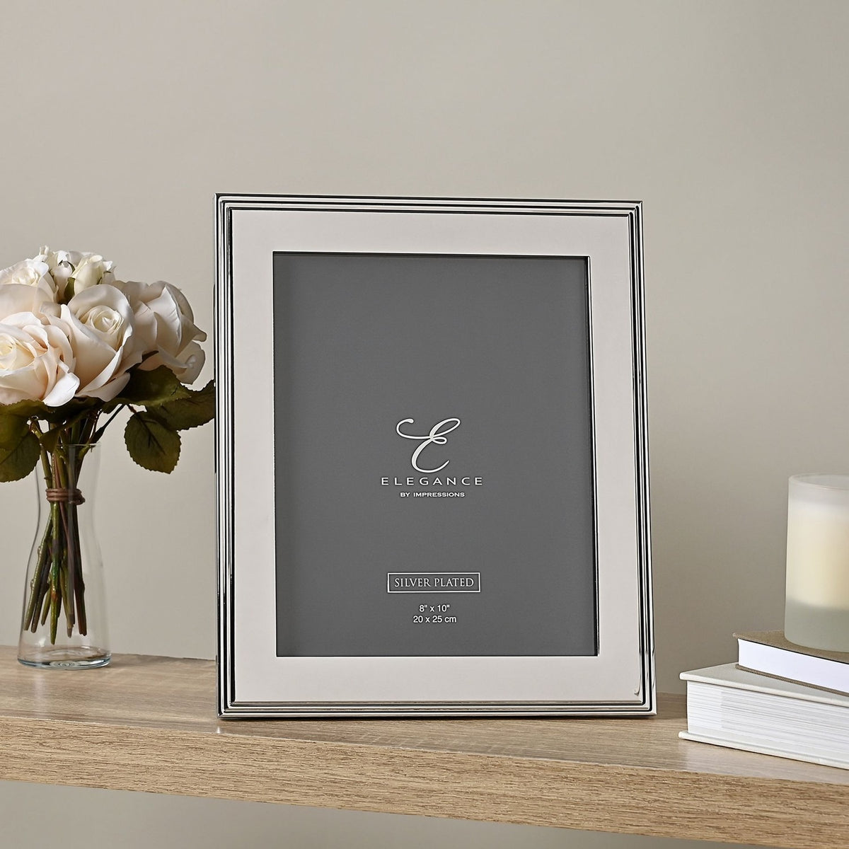Rectangular silverplated metal photo frame with ribbed stepped edge and wide flat border, displayed upright on a wooden shelf beside roses and a candle, holding an 8" x 10" print.
