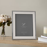Rectangular silverplated metal photo frame with ribbed stepped edge and wide flat border, displayed upright on a wooden shelf beside roses and a candle, holding an 8" x 10" print.