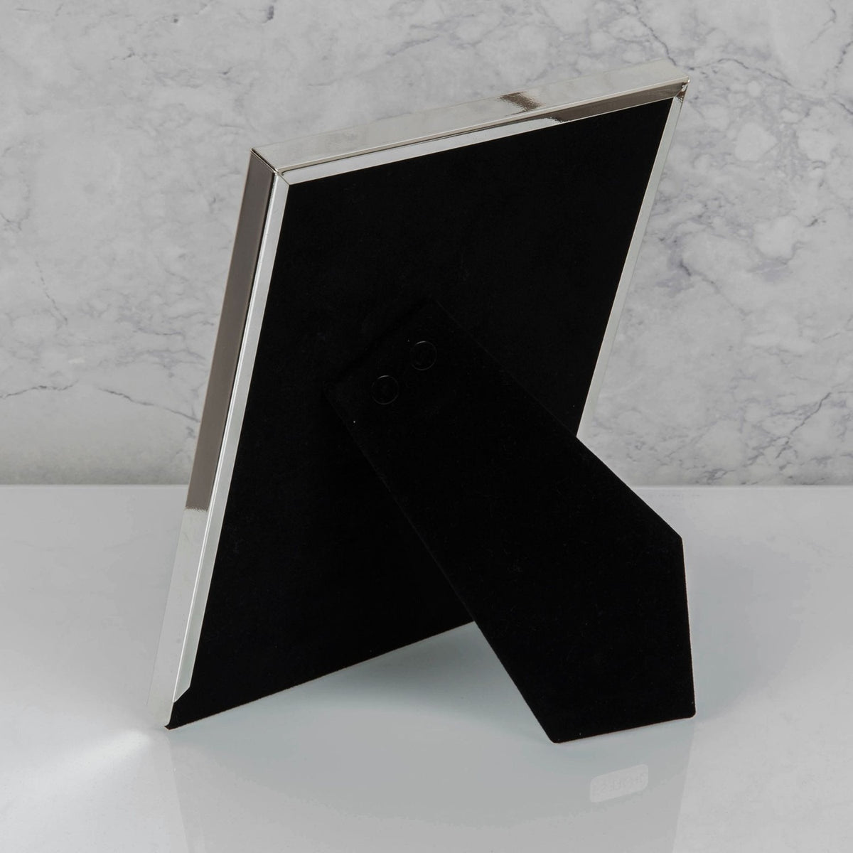 Rear view of the silverplated rib edge rectangular photo frame showing its black velvet backing and fold-out stand, set against a marble background.