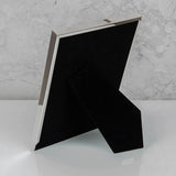 Rear view of the silverplated rib edge rectangular photo frame showing its black velvet backing and fold-out stand, set against a marble background.