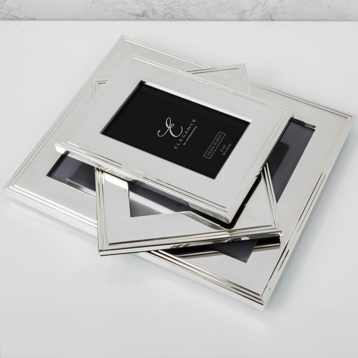 Silverplated rectangular photo frames with ribbed stepped-line borders, stacked at an angle on a white surface, one displaying a sample insert card.