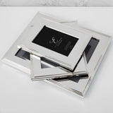 Silverplated rectangular photo frames with ribbed stepped-line borders, stacked at an angle on a white surface, one displaying a sample insert card.