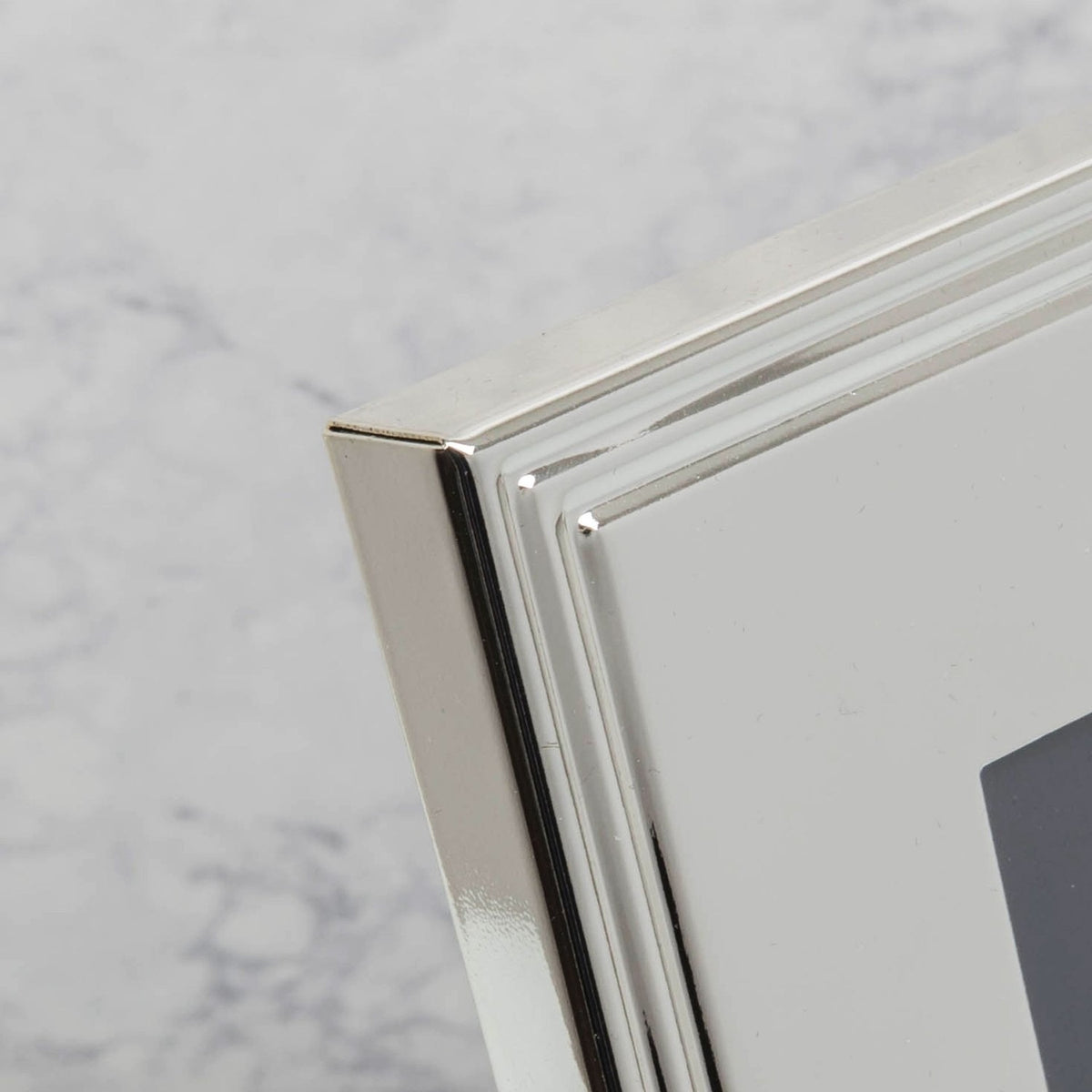 Close-up of the Gift Boxed Silverplated Rib Edge Metal Photo Frame corner, showing stepped ribbed border in polished silver finish against a marble-effect background.