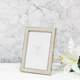 Rectangular photo frame in cream faux shagreen with a silver-tone metal edge and rear strut, shown against a marble background with a white lily.