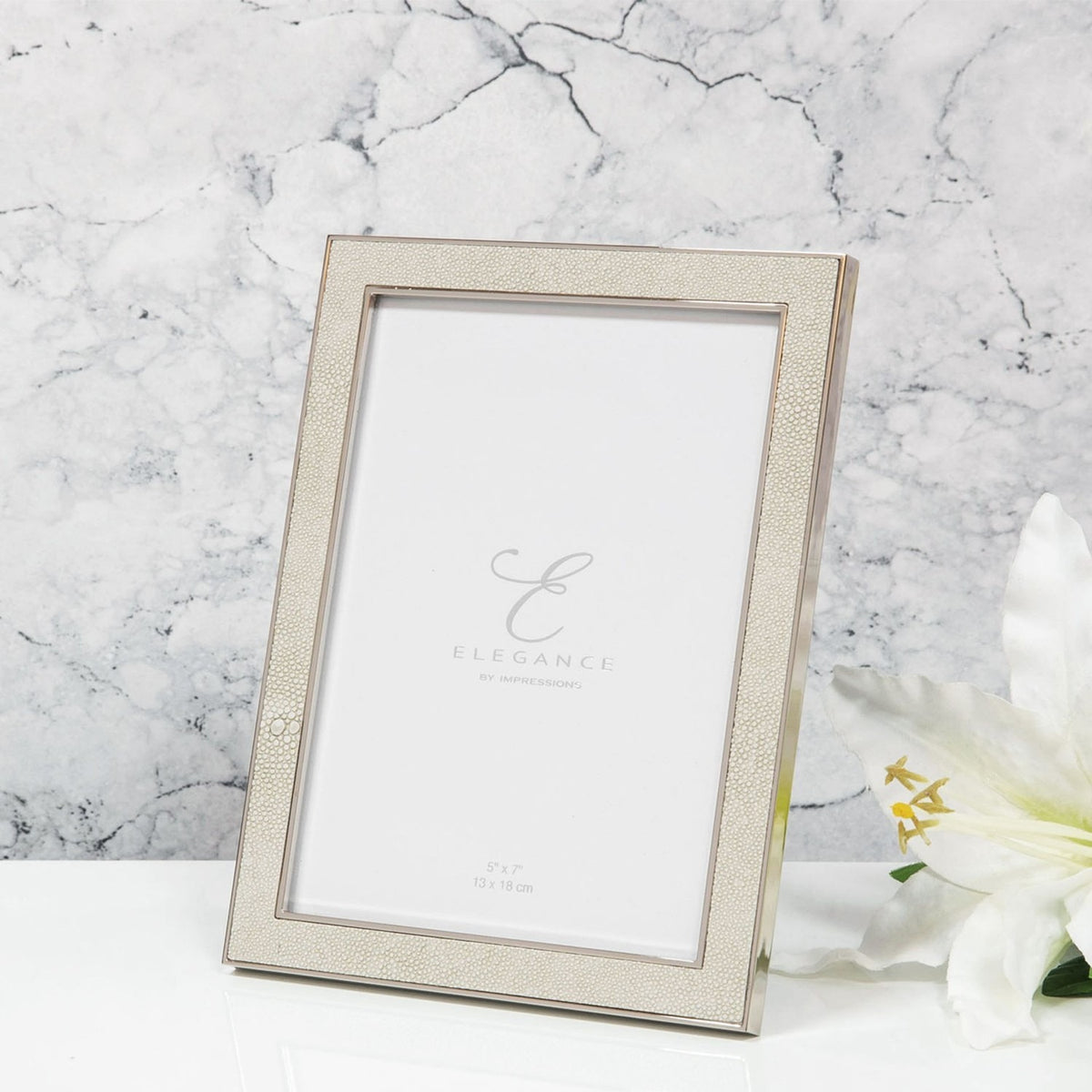 Rectangular photo frame in cream faux shagreen texture with a silver-plated metal rim, shown on a rear strut with a marble backdrop and white lily.