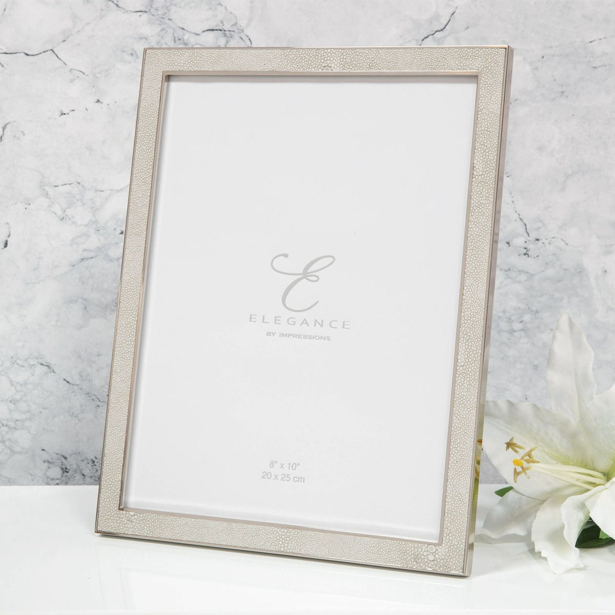 Rectangular faux shagreen photo frame in cream with a slim silver-plated metal edge and rear strut, shown on a white surface against a marble background.