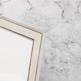 Close-up of a rectangular photo frame with cream faux shagreen pebbled texture and bright silver-plated metal edges, shown against a marble background.