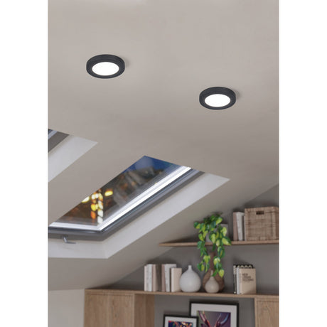 Two round Fueva Flex LED downlights with black aluminium trim and white diffusers, recessed into a sloped ceiling above a skylight in a living room.