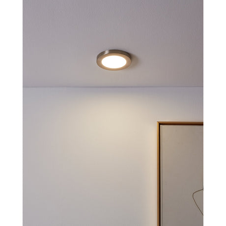 Fueva Flex round LED downlight with satin nickel rim and white diffuser, recessed in a white ceiling casting cool white light onto a wall beside a framed picture.