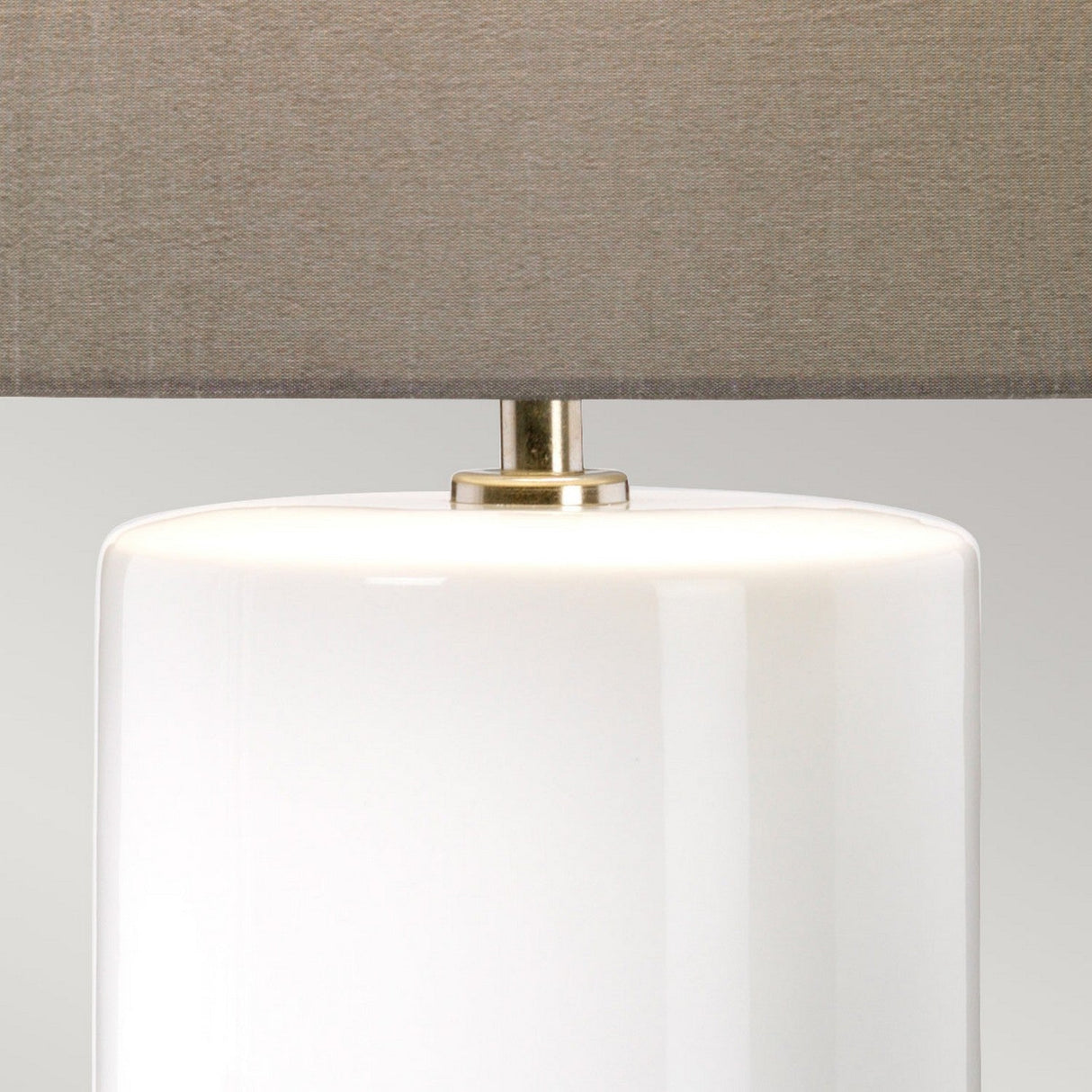 A close-up of the Fulwell 1 Light Table Lamp, featuring a sleek white glossy ceramic base paired with a matte grey fabric lampshade and an elegant brass connector, exemplifies contemporary lighting design.