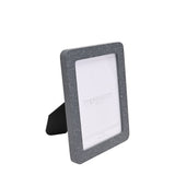 Speckled rounded wooden photo frame in grey with fine white flecks, rectangular with rounded corners, holding a 7 x 5in print, shown at an angle on a plain white background.