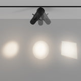 The Gala CCT Dimmable LED Magnetic Exility Track Spotlight 10W 2700-6000K in black features three adjustable lamps that project unique shapes—two round and one square—onto a gray surface. CCT dimmable technology allows varying brightness and clarity of the light beams.