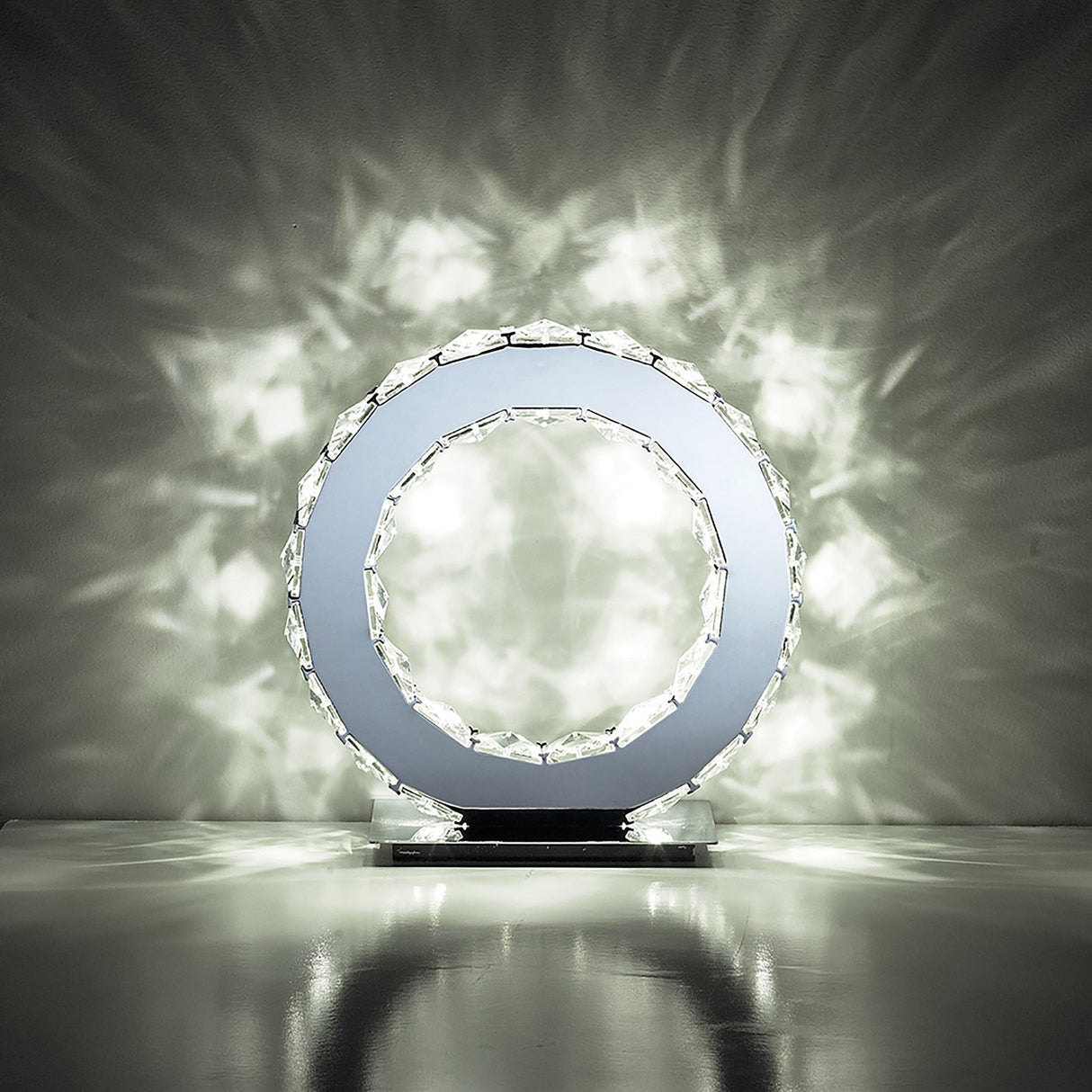 The Galaxy LED Crystal Round Table Lamp 10W 6000K in polished chrome features a crystal-like outer ring that casts bright, decorative light patterns on walls and surfaces, adding a sparkling effect to any dark room.