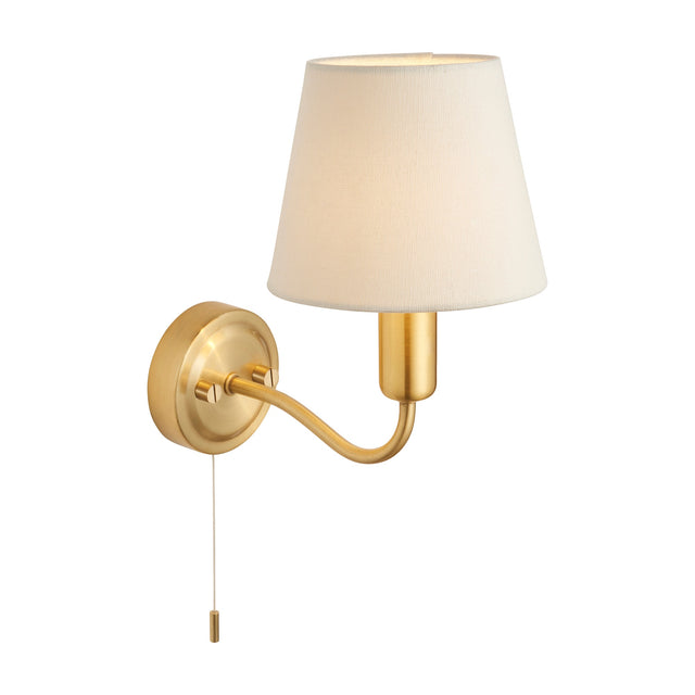 Gallery Direct Convaine bathroom wall light in brushed brass with curved arm, cream tapered fabric shade, and pull cord switch on a white background.