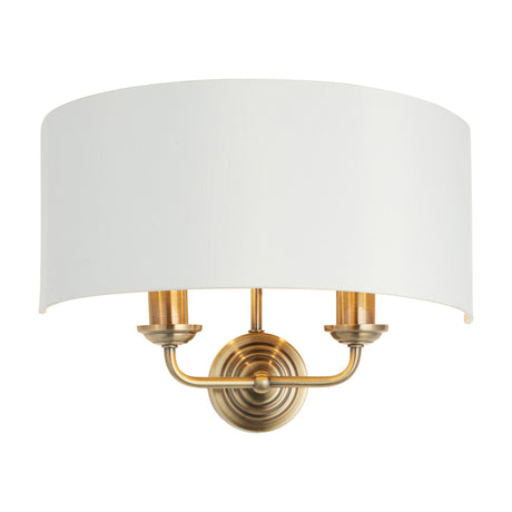 Gallery Direct Clervorne 2 Light Wall Light with antique brass twin arms, turned backplate and white half-drum fabric shade on a plain background.