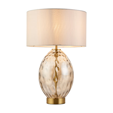 Gallery Direct Elrisse table lamp with dimpled champagne oval glass body, brushed brass base and neck, and cream fabric drum shade.