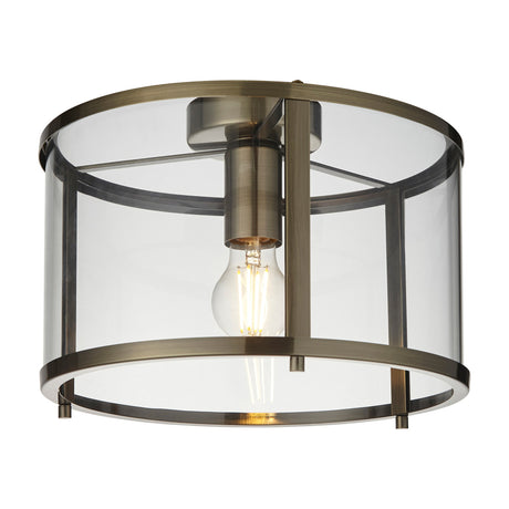 Gallery Direct Hoplora Flush Ceiling Light in antique brass with a clear glass drum shade and single E27 filament bulb, on a white background.