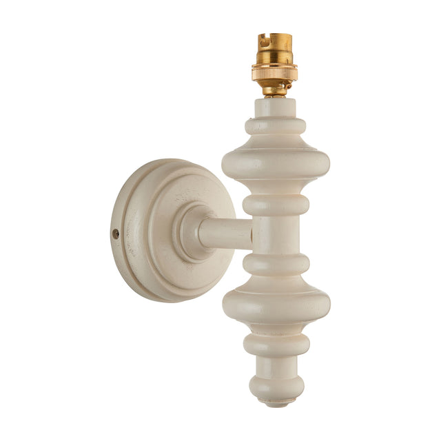 Gallery Direct Carnvenne turned wooden wall light fitting in almond white with spindle body, round backplate and brass B22 lampholder on a plain background.