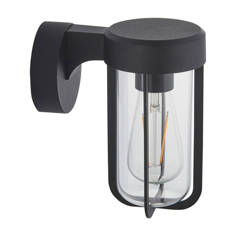 Gallery Direct Luvenna wall light in textured black with die cast aluminium frame, curved bracket and clear glass cylinder shade housing a filament bulb.